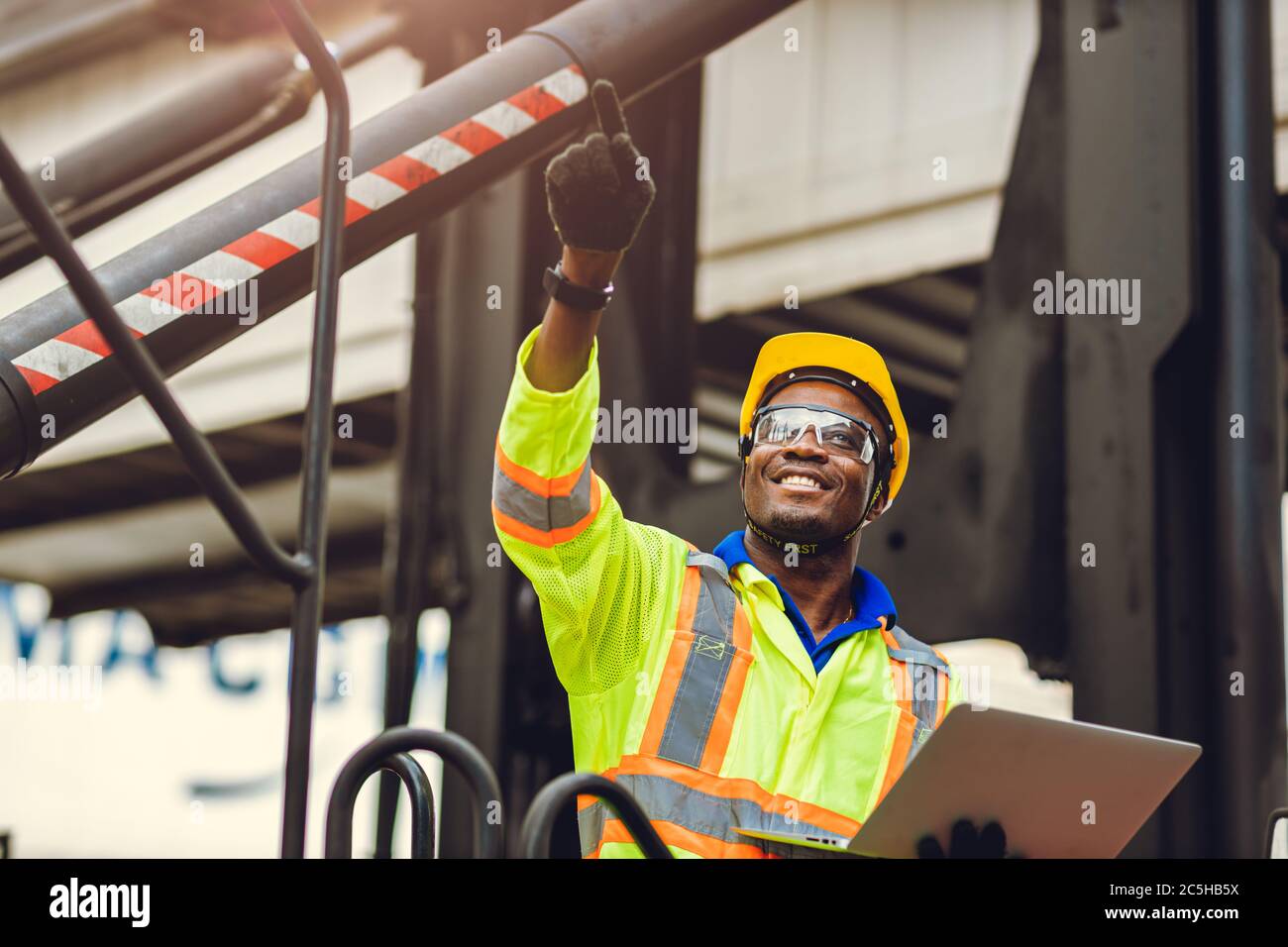 Lavoratore nero afroamericano come caposquadra orgoglioso di felice sorriso di lavoro controllo carico carico carico in magazzino logistica di spedizione con tuta di sicurezza. Foto Stock