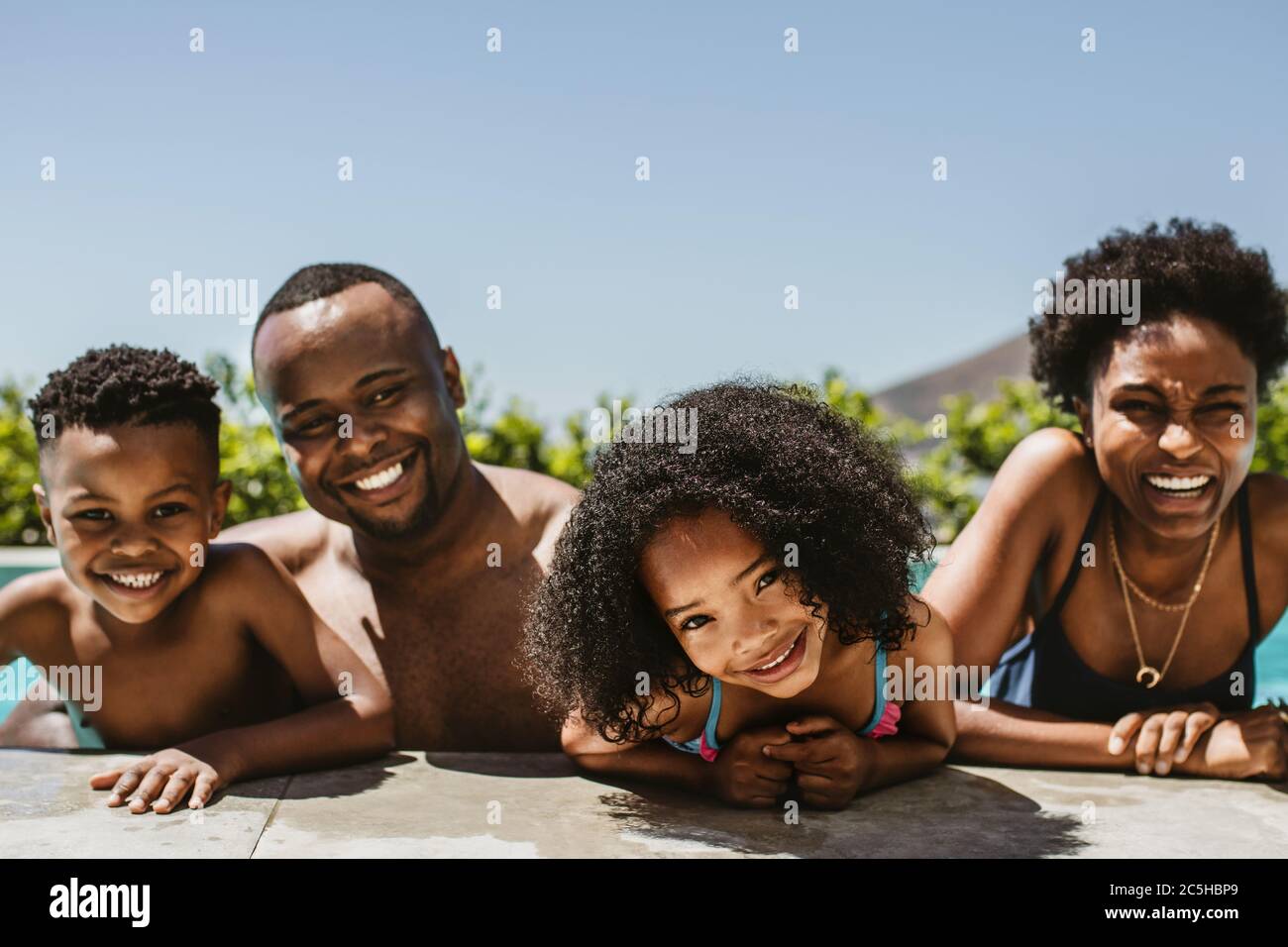 Felice giovane famiglia in piscina in una giornata estiva. Famiglia di quattro persone che si godono la loro vacanza estiva. Foto Stock