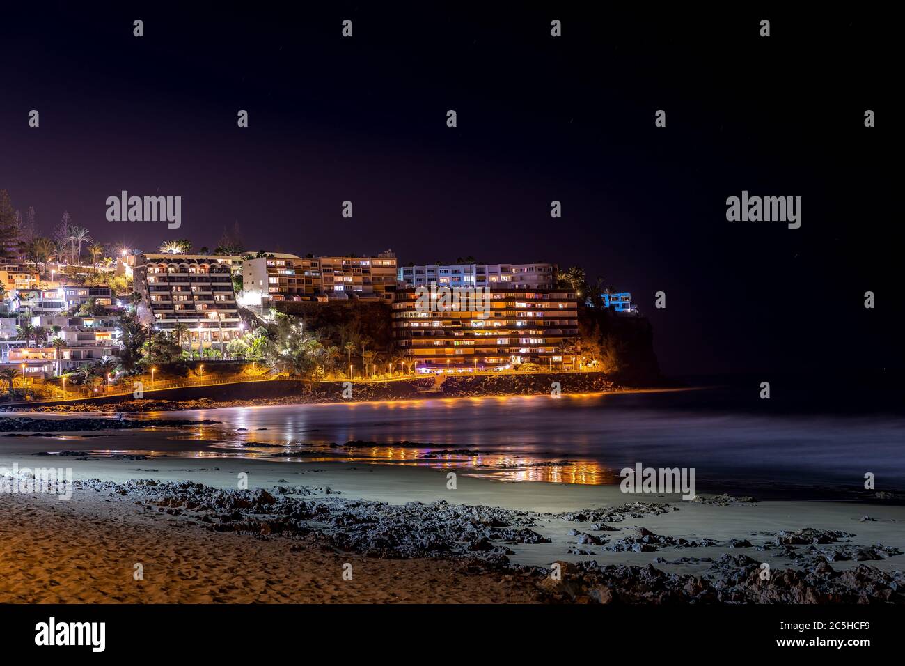 Vista della città notturna sulla scogliera di roccia catturata durante la sera con il riflesso delle ombre sulla superficie dell'oceano e altri riflessi di luce di strada sulla superficie. Foto Stock