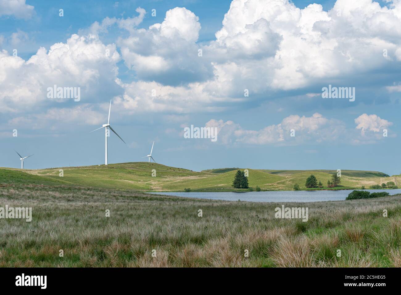 Alcune turbine eoliche su una collina scozzese sopra un piccolo bacino idrico interno con un cielo limpido e blu nuvoloso a giugno. Foto Stock