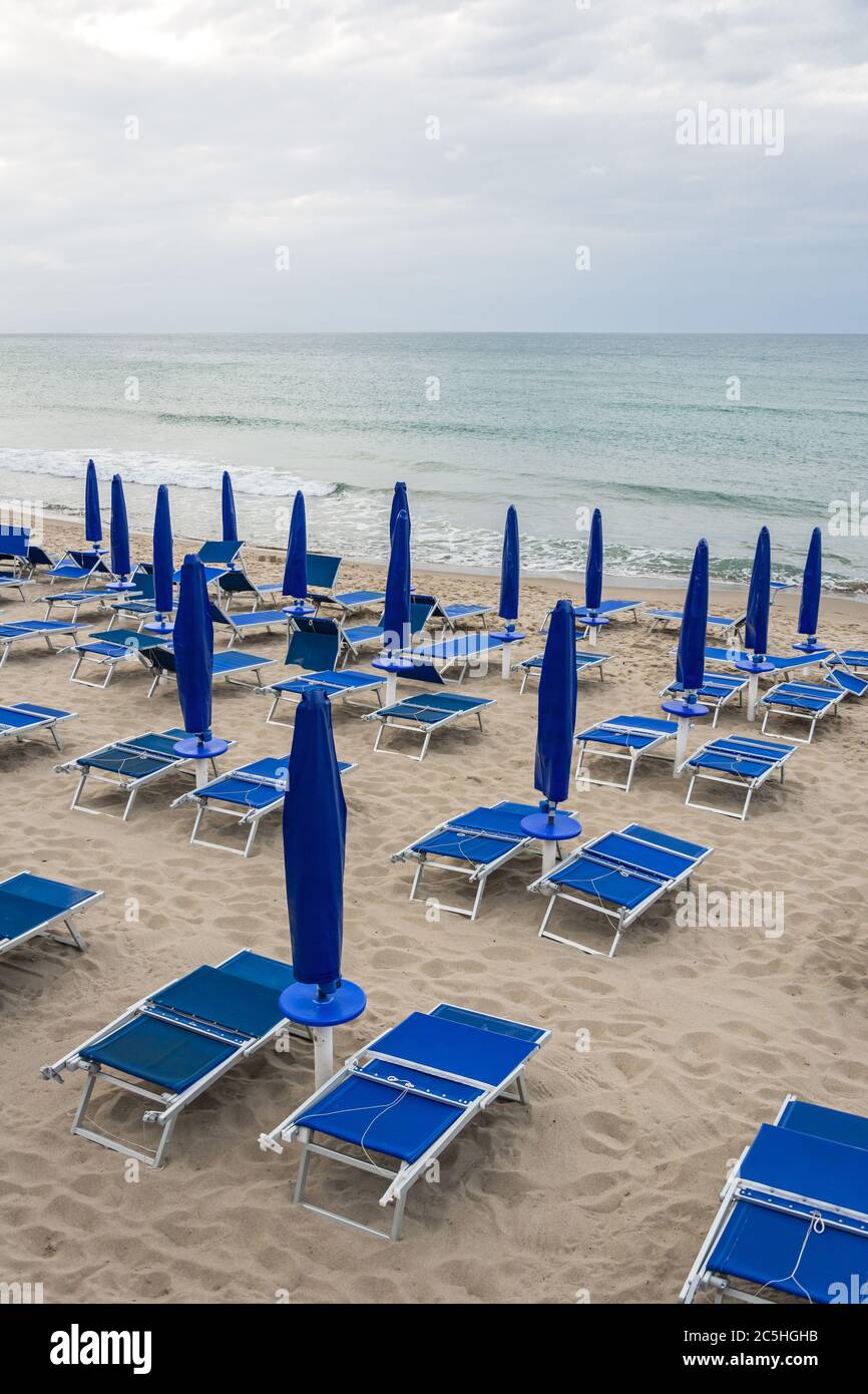 Lettini e ombrelloni vuoti sulla spiaggia deserta durante la bassa stagione Foto Stock