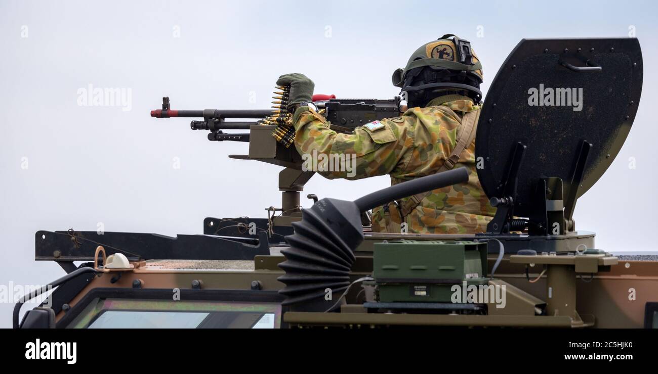 Soldato dell'esercito australiano con una grande mitragliatrice nella torretta di un portatore di personale blindato Bushmaster (APC). Foto Stock