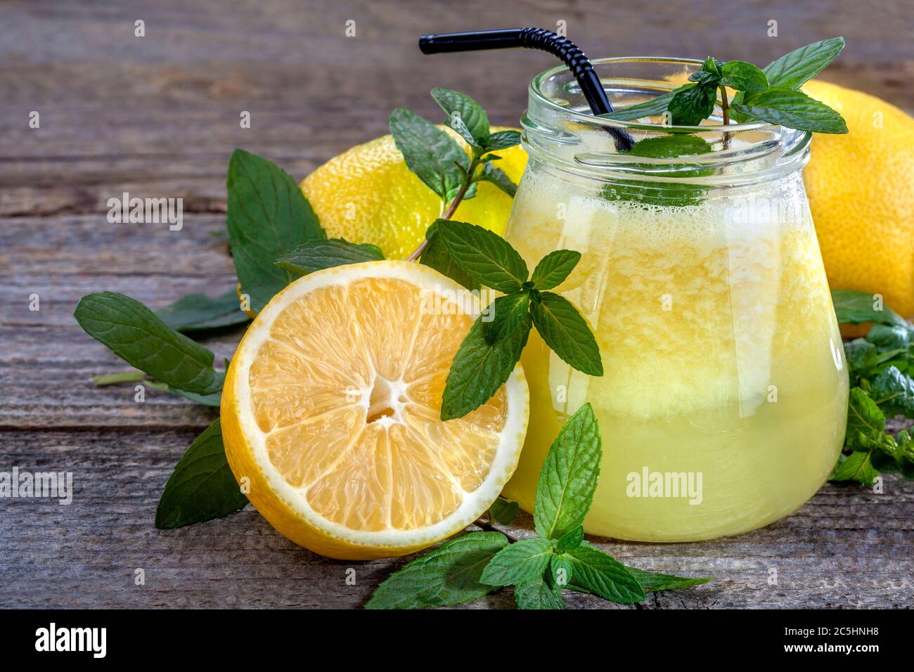 Succo di limone appena spremuto con menta. 100% succo di limone con polpa e frutta a fette e menta come decorazione su tavola rustica di legno. Foto Stock