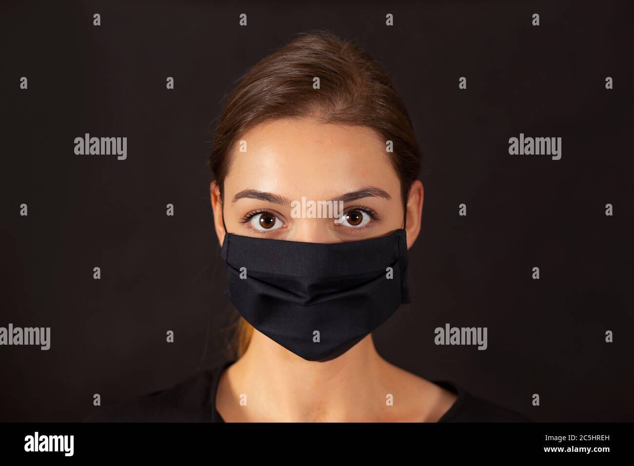 Primo piano di una ragazza che indossa una maschera nera del viso in tessuto durante una pandemia di Covid-19. Foto Stock