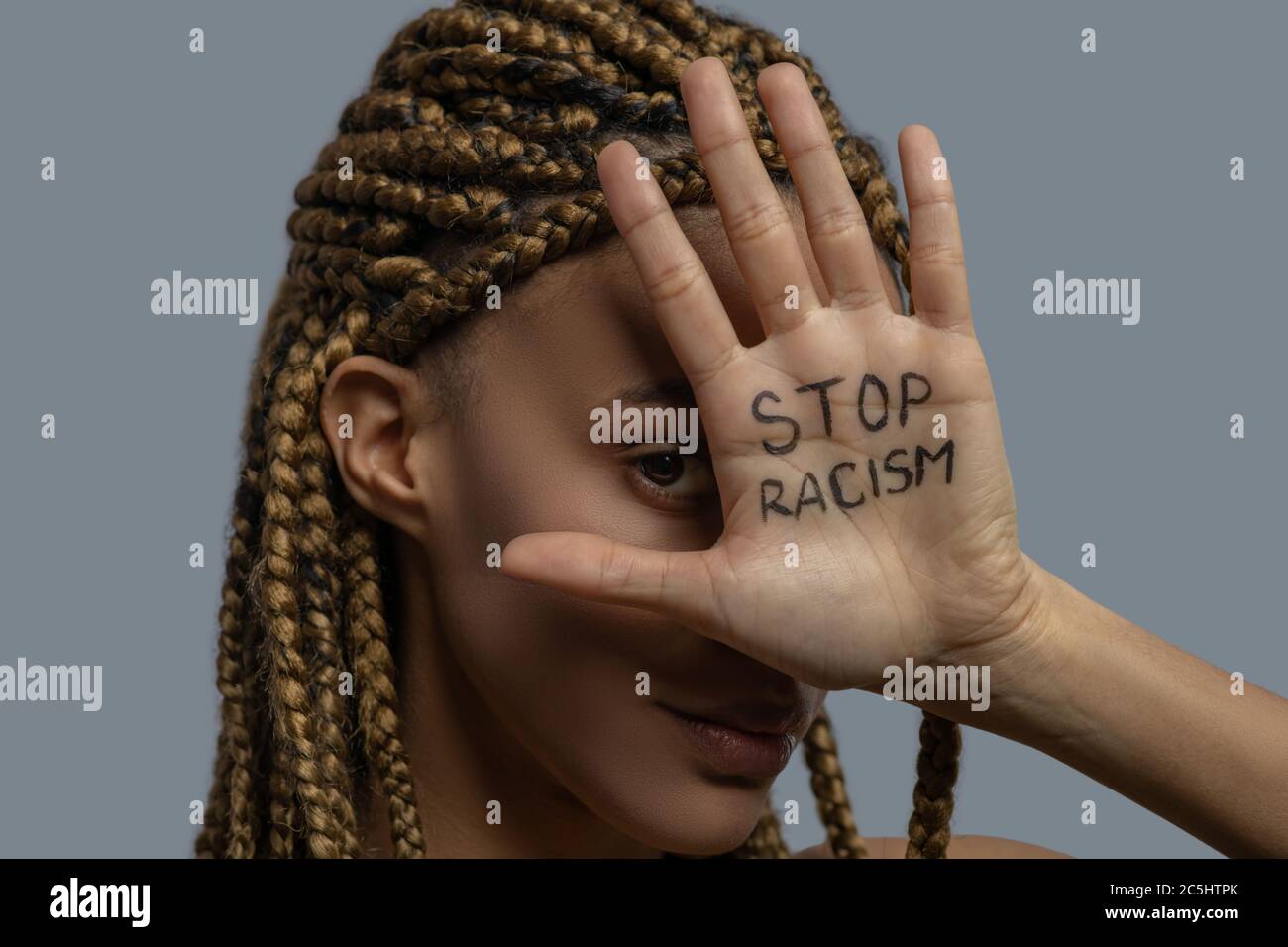 Giovane donna afroamericana che ricopre il suo occhio con palma con lettere di stop razzismo Foto Stock