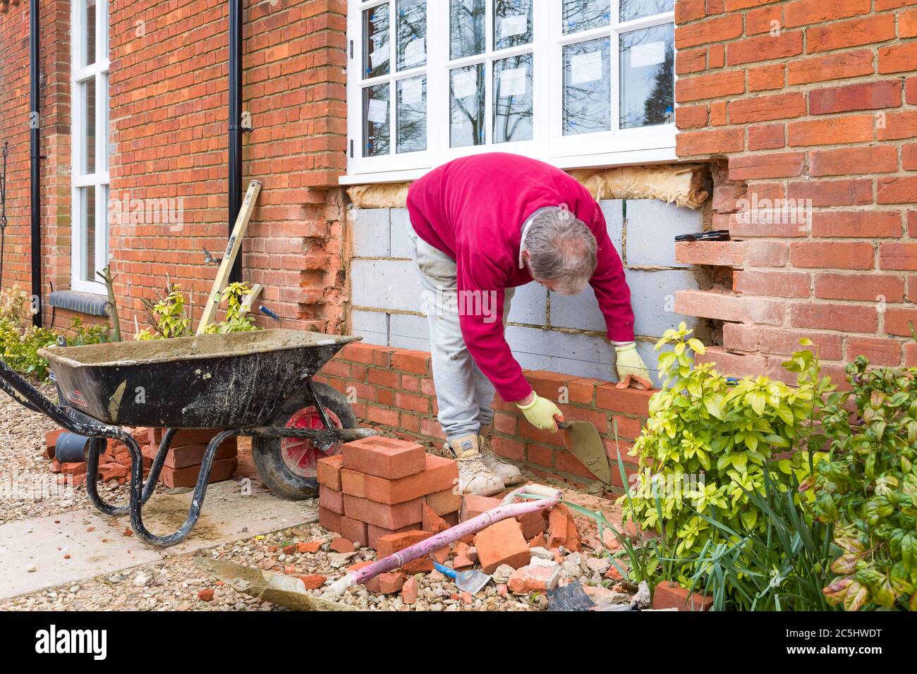 BUCKINGHAM, Regno Unito - 15 marzo 2016. Muratore che costruisce un muro su una casa del patrimonio britannico mentre installa le finestre di legno di ricambio. Miglioramento domestico, prop Foto Stock