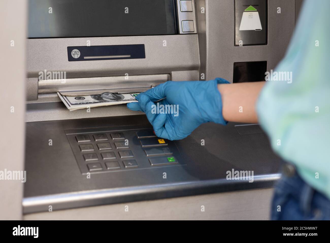 Mano femminile in guanto medico protettivo che prende denaro dalla macchina ATM Foto Stock