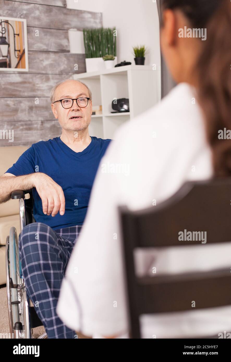 Anziano in sedia a rotelle che parla con l'infermiere del suo problema medico. Disabilità anziano con operatore medico in assistenza infermieristica a domicilio, assistenza sanitaria e medicina. Foto Stock