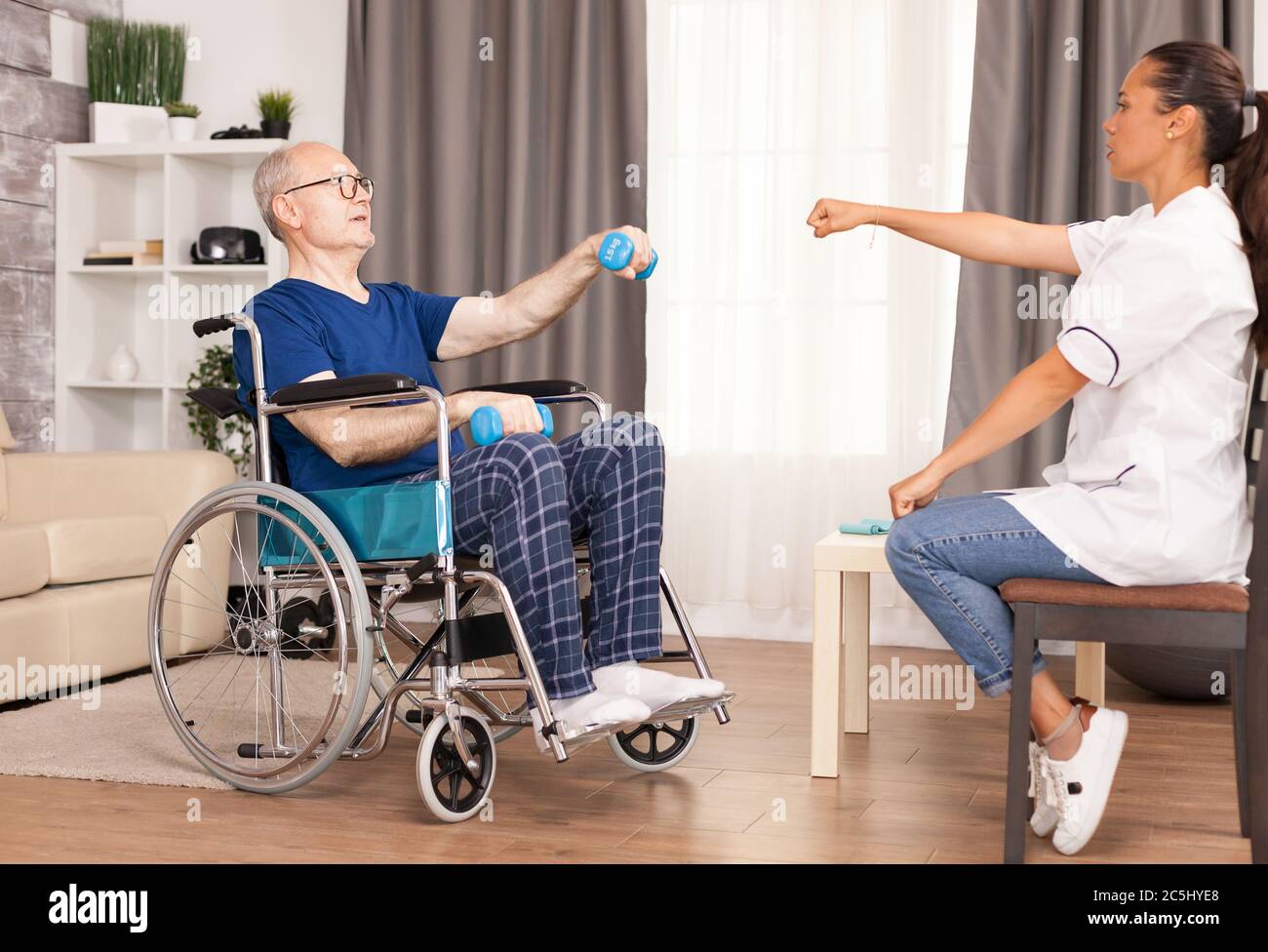 Uomo in sedia a rotelle che si esercita con manubri per il recupero. Disabilità anziano con operatore medico in assistenza infermieristica a domicilio, assistenza sanitaria e medicina Foto Stock