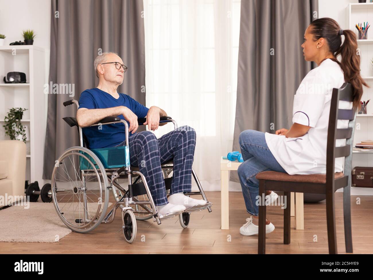 Persona in sedia che parla con l'infermiere nell'ufficio del medico. Disabilità anziano con operatore medico in assistenza infermieristica a domicilio, assistenza sanitaria e medicina Foto Stock