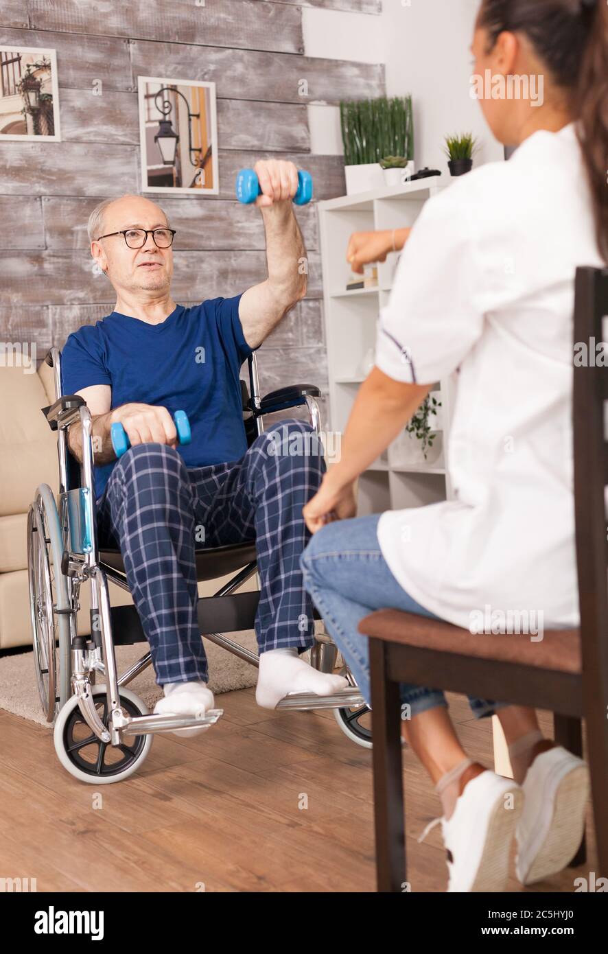 Nonno in sedia a rotelle che fa sport assistito da infermiera. Disabili anziani disabili con lavoratore sociale in recupero terapia di supporto fisioterapia sistema sanitario di cura casa di riposo Foto Stock