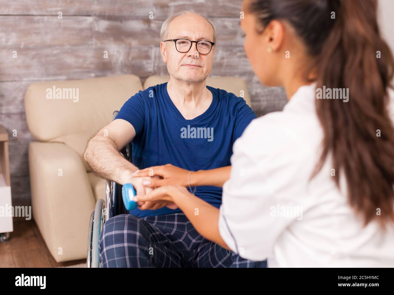 Caregiver aiutare l'uomo paralizzato a recuperare utilizzando manubri per i muscoli delle braccia. Disabili anziani disabili con lavoratore sociale in recupero terapia di supporto fisioterapia sistema sanitario di cura casa di riposo Foto Stock