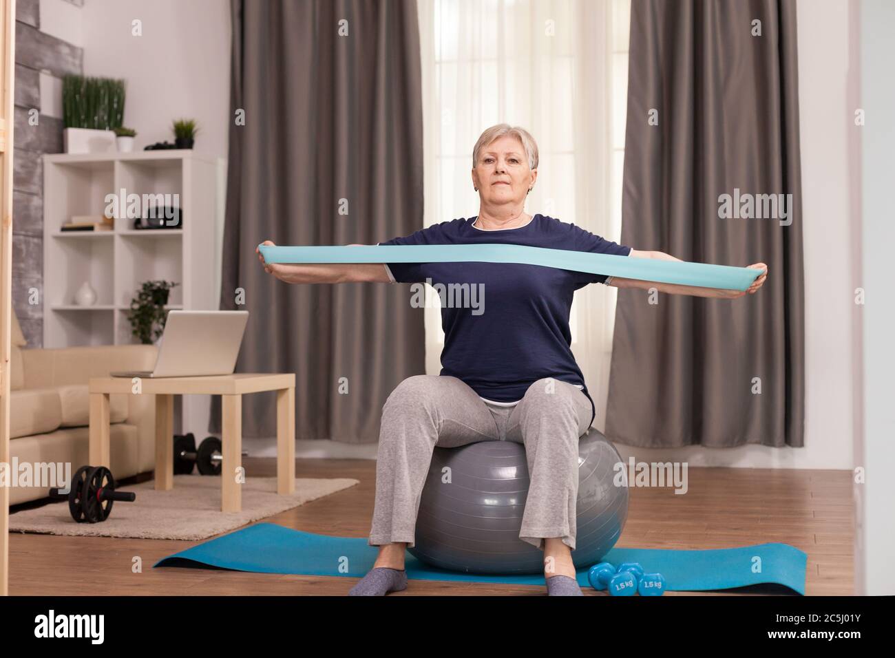 Donna ambiziosa che fa sport a casa con la banda Resistance. Anziano pensionato online internet esercizio di formazione a casa attività sportiva con manubri, banda di resistenza, palla svizzera all'età di anziano pensionamento Foto Stock