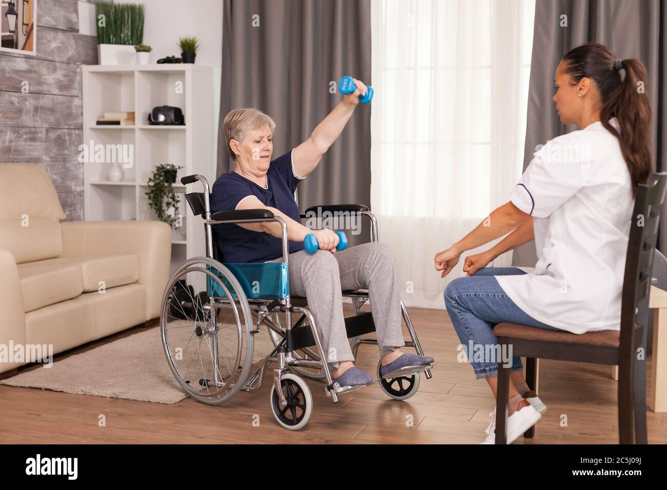 Donna anziana non valida che usa pesi con l'aiuto di un infermiere. Disabili anziani ricoverati infermiere professionista di aiuto, cura casa di riposo e riabilitazione Foto Stock