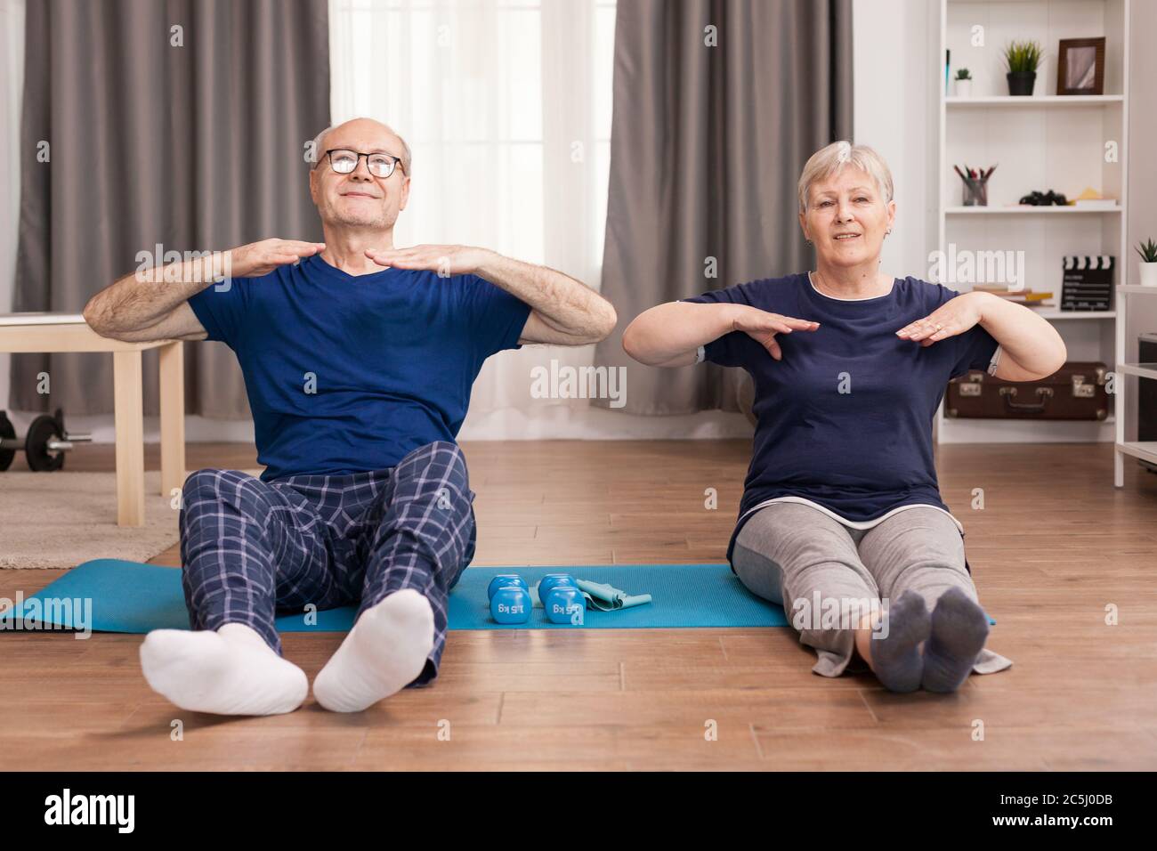 Persone anziane che hanno uno stile di vita sano che fanno sport in salotto. Esercizio di stile di vita sano in casa, allenamento e allenamento, attività sportive a casa su tappetino yoga. Foto Stock