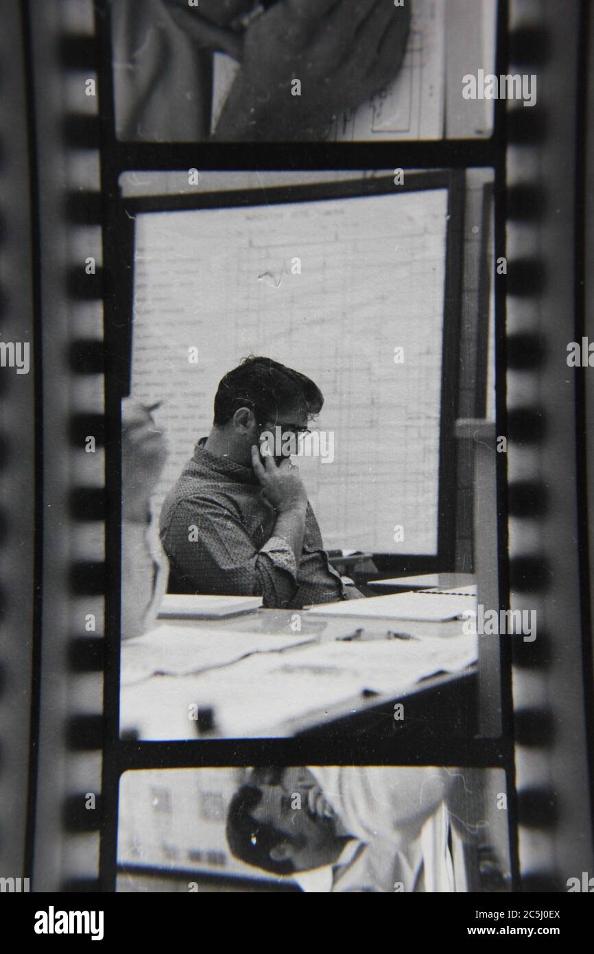 Fine anni '70 vintage contatto stampa in bianco e nero fotografia di un uomo che scrive su un sacco di documenti. Foto Stock