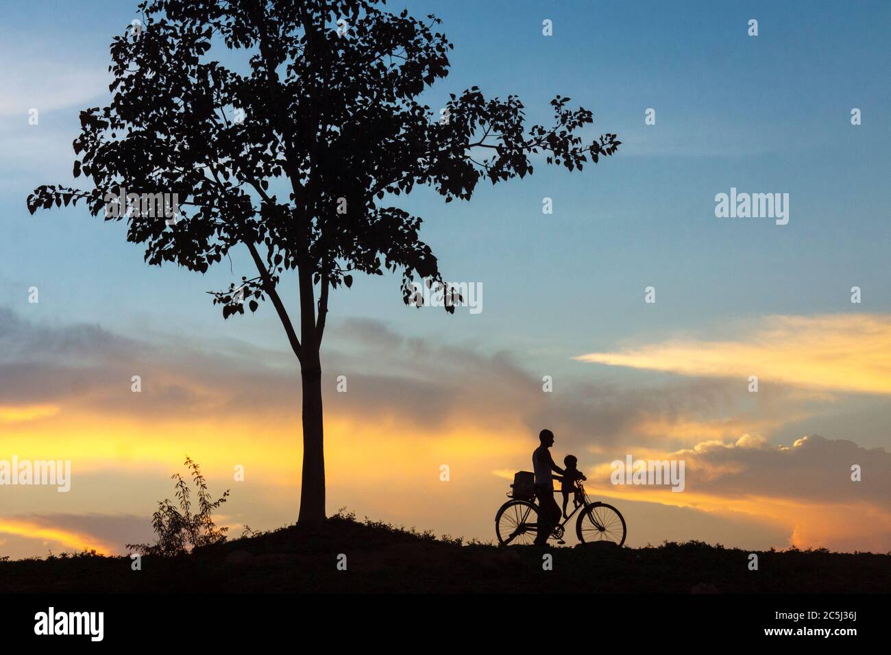 Khajuraho, Madhya Pradesh, India : UN uomo e un bambino prendono un idilliaco giro in bicicletta al tramonto. Foto Stock