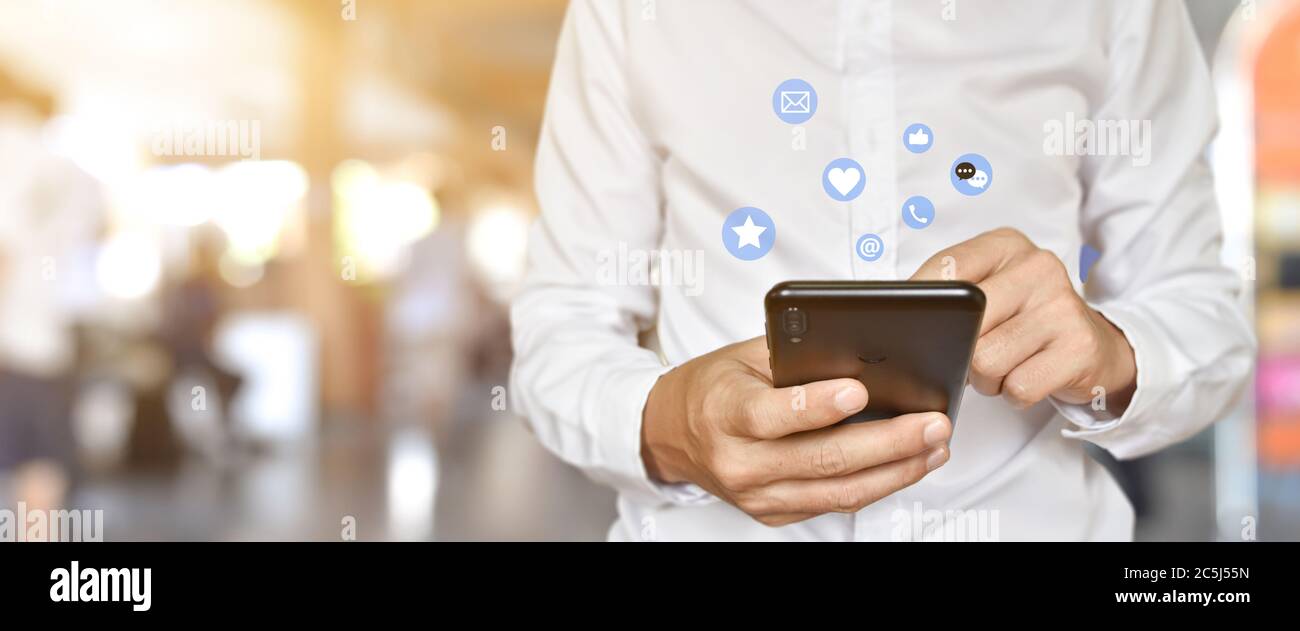 Primo piano di un uomo che utilizza lo smartphone mobile con icone social e multimediali. Concetto di tecnologia di marketing o aziendale. Foto Stock