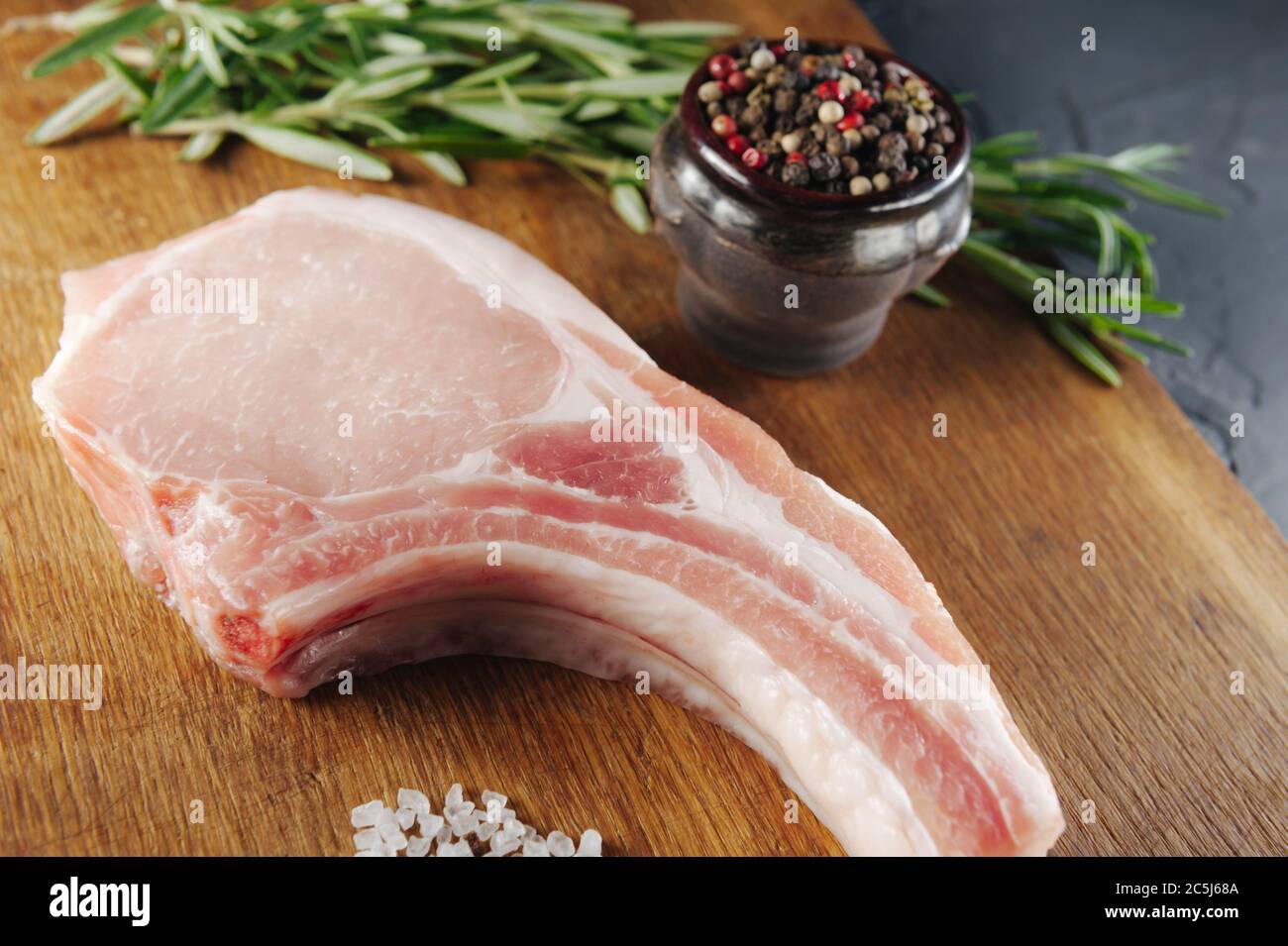 un bel pezzo di carne cruda con spezie su un asse di legno con sale e pepe Foto Stock