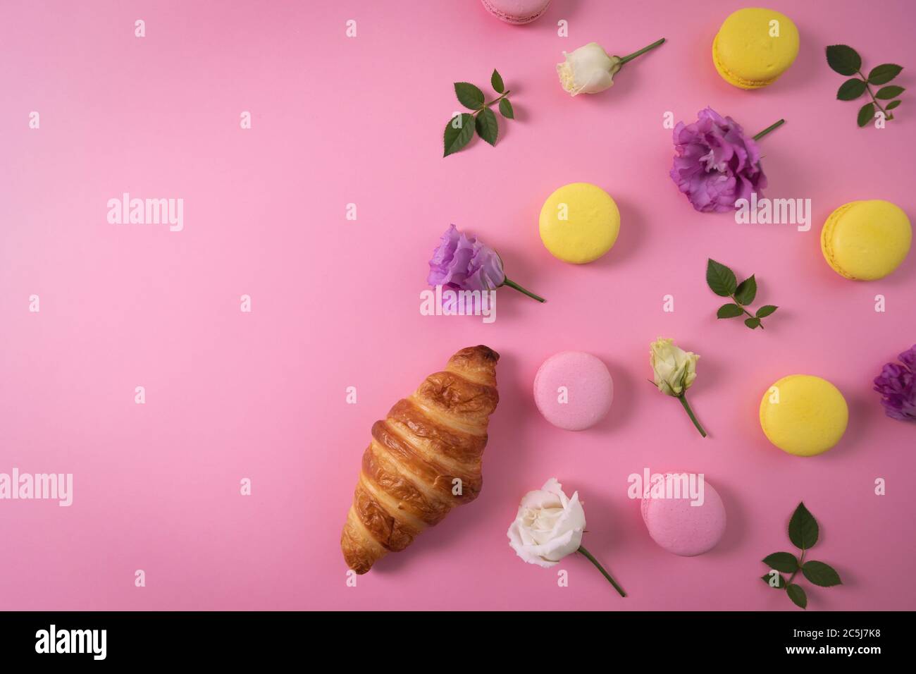 pasticceria francese - macaron e croissant con fiori su sfondo rosa con spazio copia. vista dall'alto Foto Stock