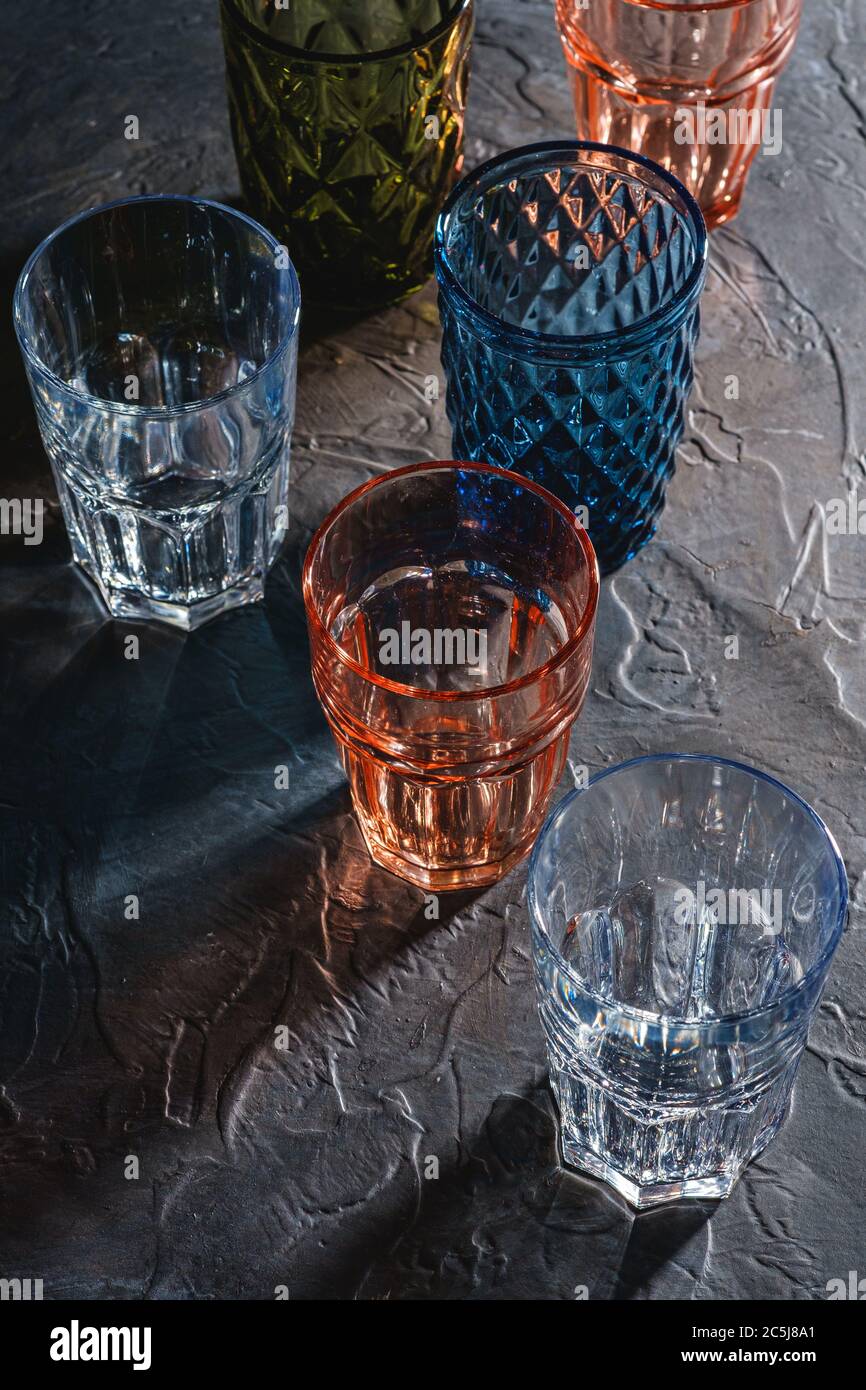 Bicchiere colorato sfaccettato e geometrico, gruppo di bevande verdi, rosse, blu e trasparenti per bevande su fondo di cemento in pietra scura, Foto Stock