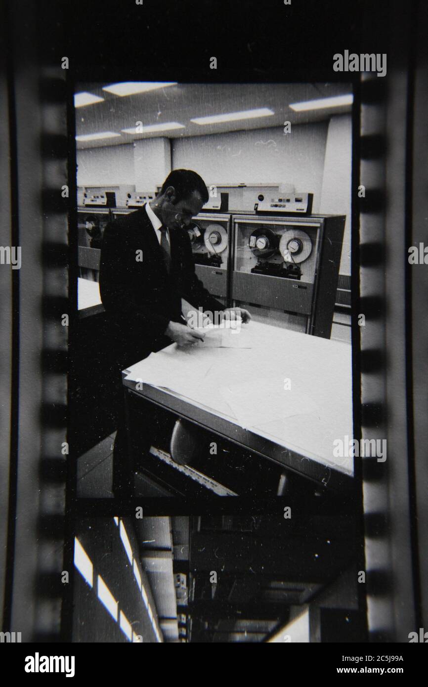 Fine anni '70 vintage contatto stampa in bianco e nero fotografia di un uomo che sovrintende un computer in una sala computer. Foto Stock