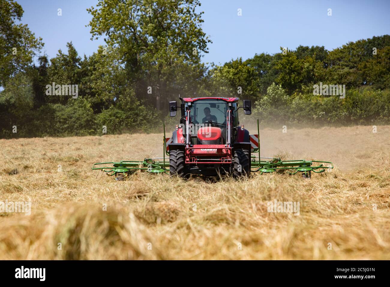 Hay Harvest giugno 2020 trattore rosso Regno Unito, tornando fieno in preparazione per imballarlo, cielo blu bella giornata di sole. Fare fieno mentre il sole splende. Hampshire Regno Unito Foto Stock