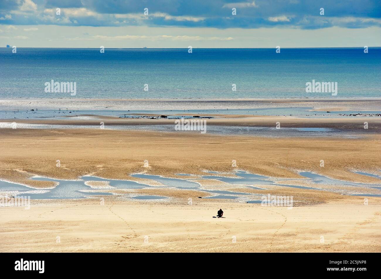 Figura solitaria vestita di nero sedette sulla spiaggia sotto il cielo tempestoso Foto Stock
