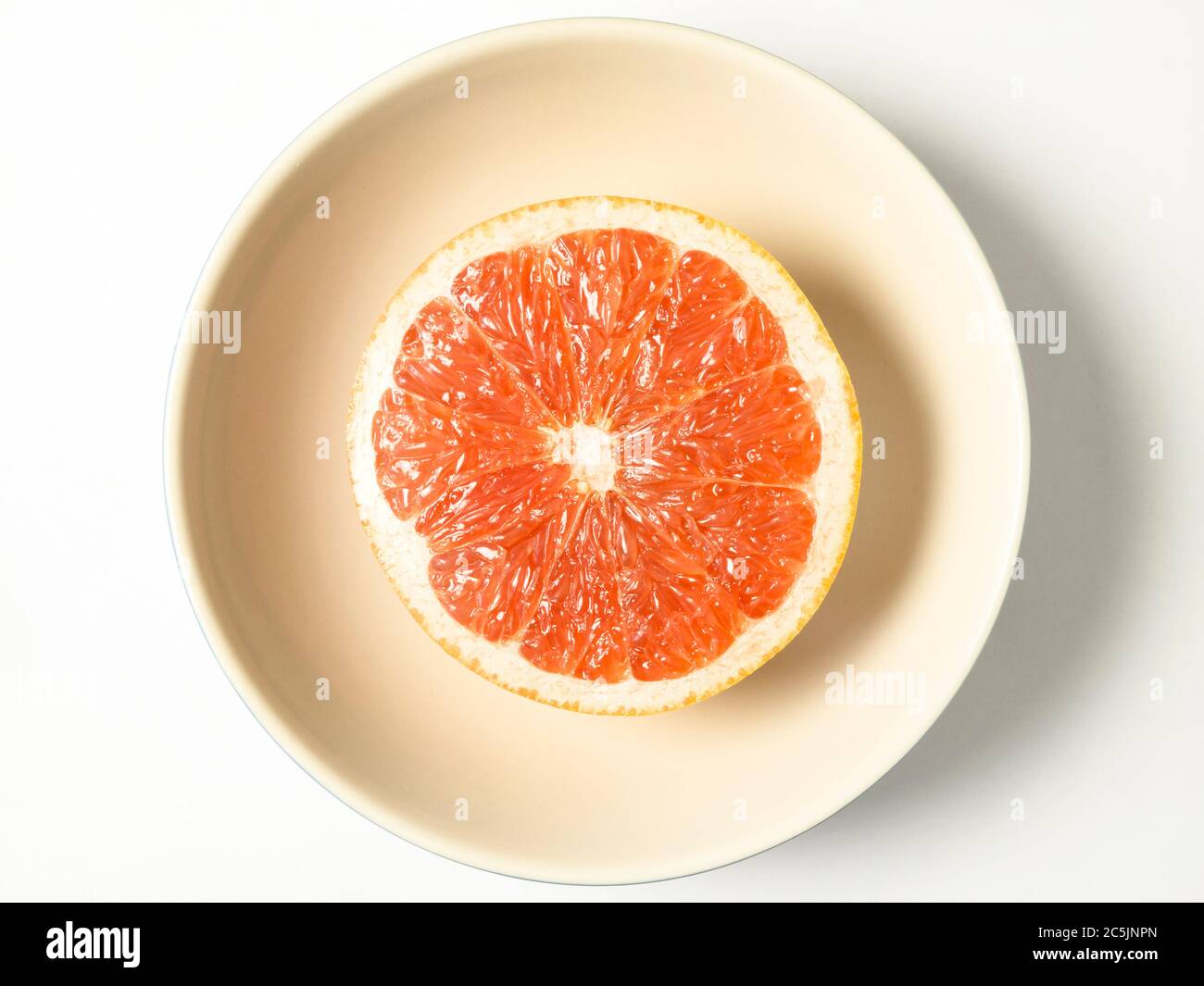 Mezzo pompelmo rosa in una ciotola centrata su uno sfondo bianco Foto Stock