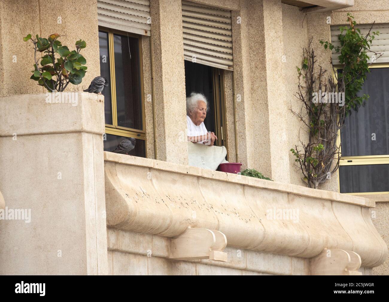 Donna anziana che guarda fuori dalla finestra dell'appartamento in Spagna. Foto Stock