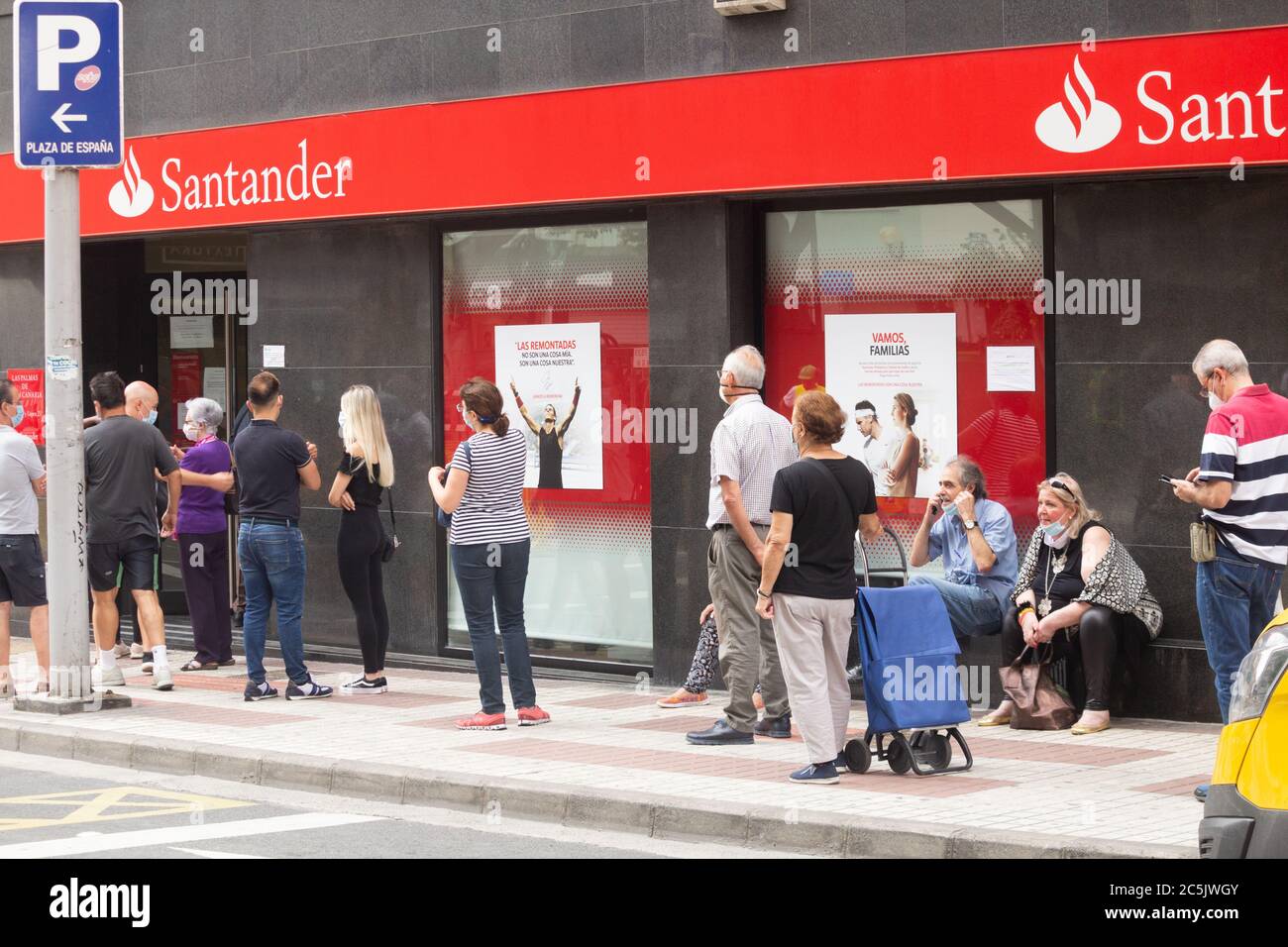 Persone che indossano maschere facciali in coda fuori della banca Santander durante Covid 19, pandemia di Coronavirus in Spagna Foto Stock