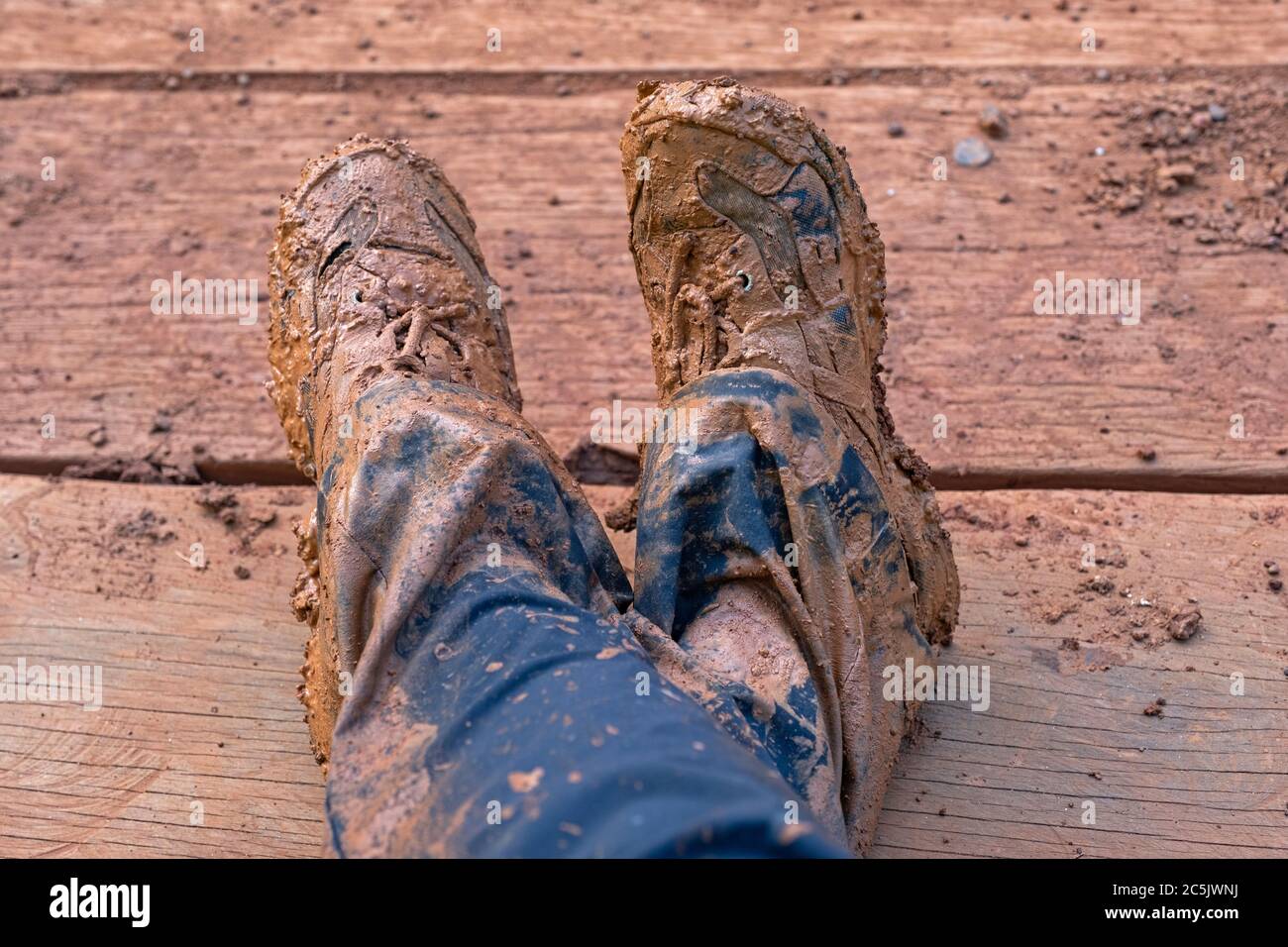 Primo piano di scarpe e pantaloni umidi, sporchi e fangosi ricoperti di fango rosso Foto Stock