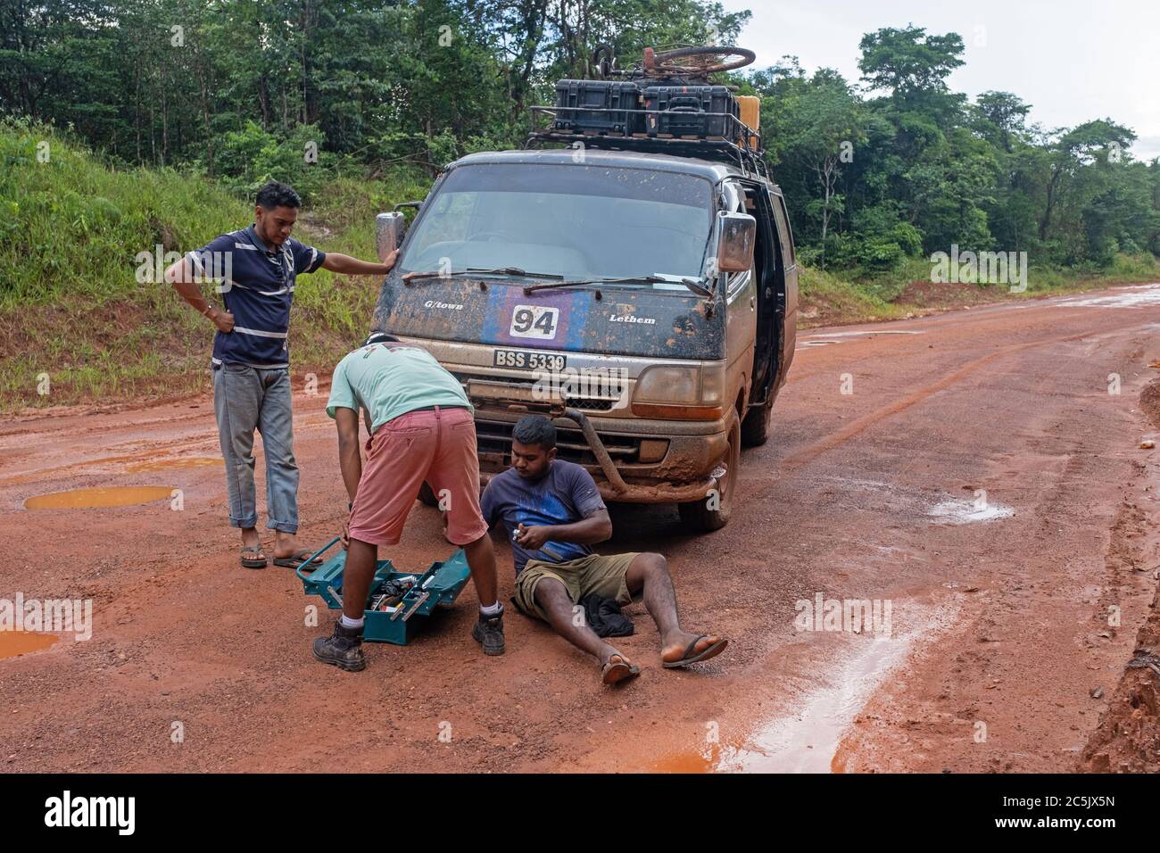 Autista che ripara minibus rotto nella foresta pluviale lungo la strada sterrata Linden-Lethem che collega Lethem e Georgetown, Guyana, Sud America Foto Stock