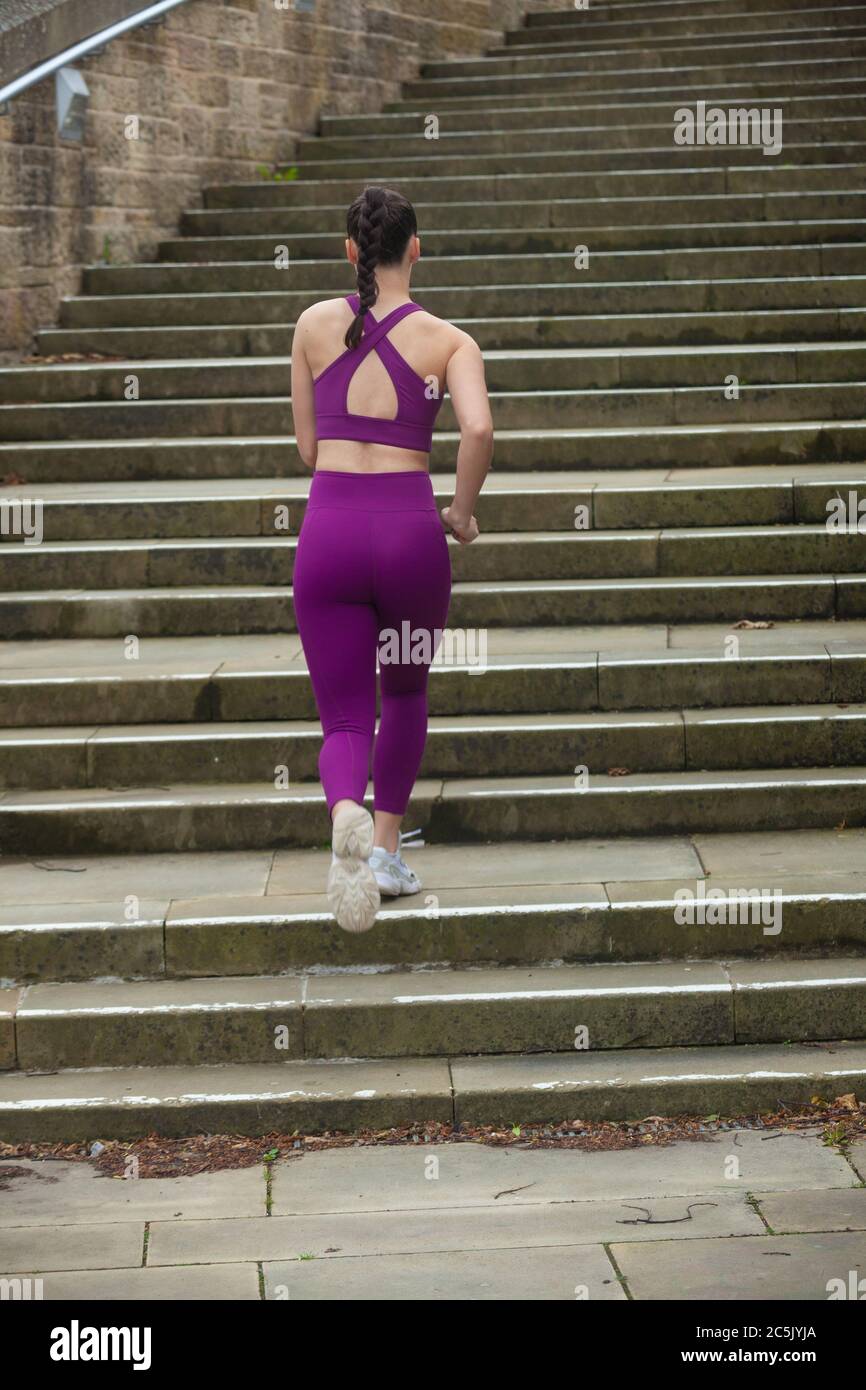 Una vista posteriore di una giovane donna che indossa abiti sportivi che corrono su gradini di cemento Foto Stock