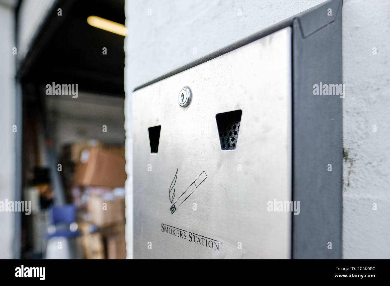 Fuoco superficiale di un contenitore di sigarette usato in metallo visto attaccato ad una parete esterna, all'entrata di un magazzino. Foto Stock