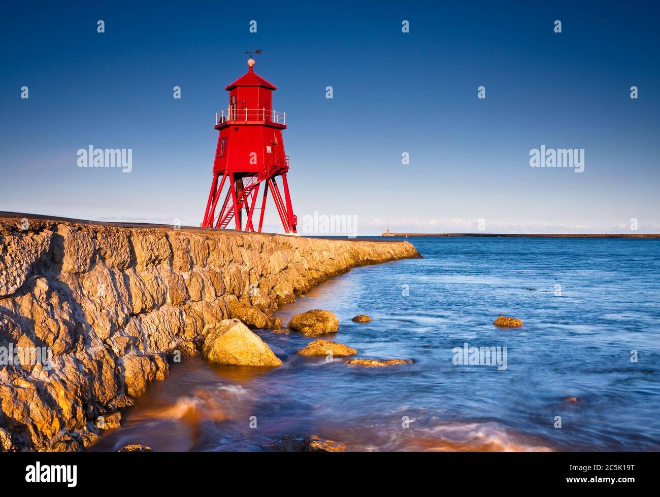 Guardando lungo il molo di roccia verso il faro rosso a South Shields in una serata di inizio estate Foto Stock