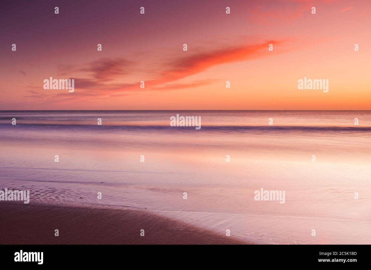 Una tranquilla e calda vista colorata sulla spiaggia e sulla baia che guarda verso l'orizzonte e ondulati onde che si lavano sulla spiaggia. Foto Stock