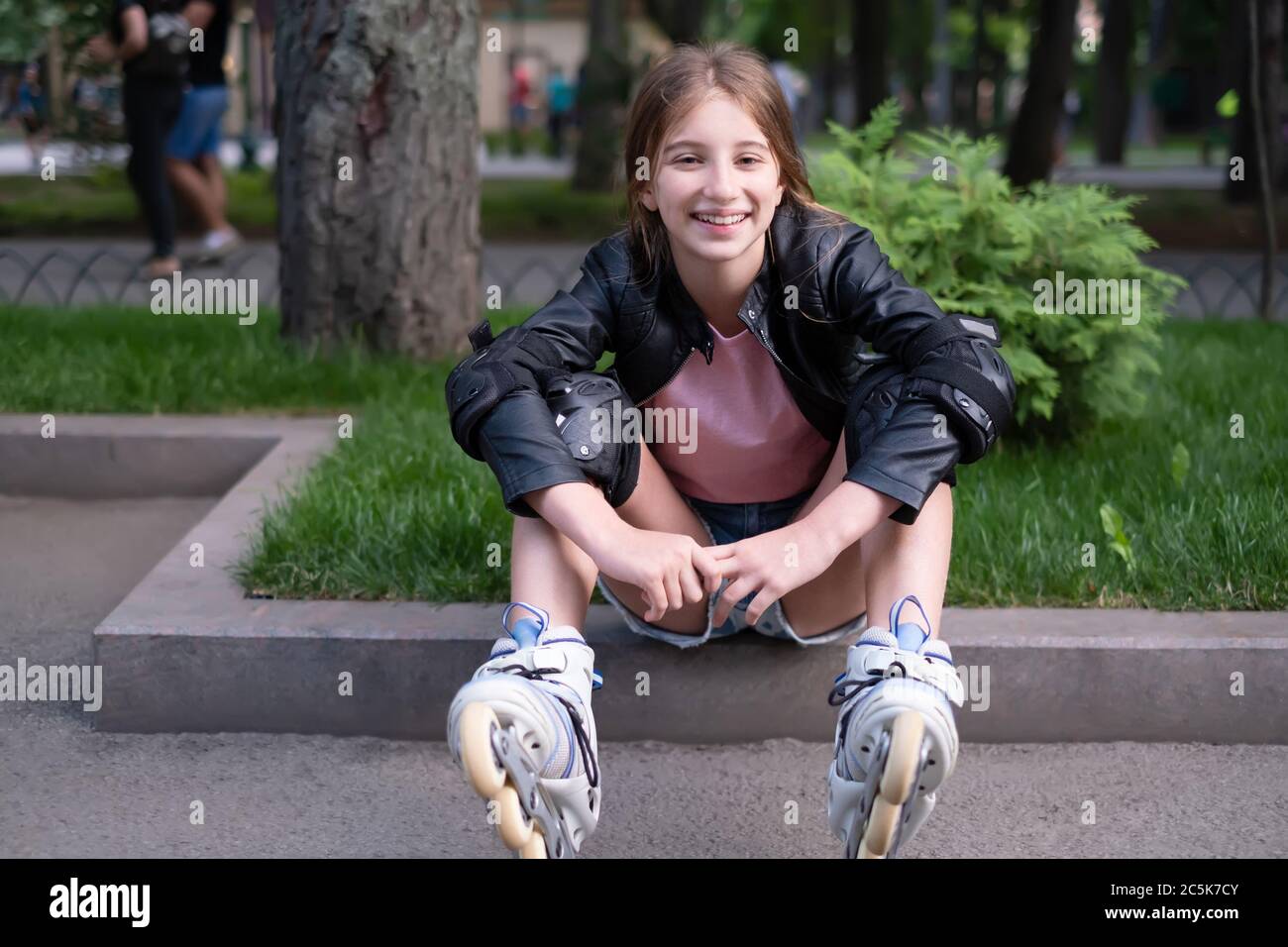 Sorridente giovane seduta in pattini a rotelle del parco Foto Stock