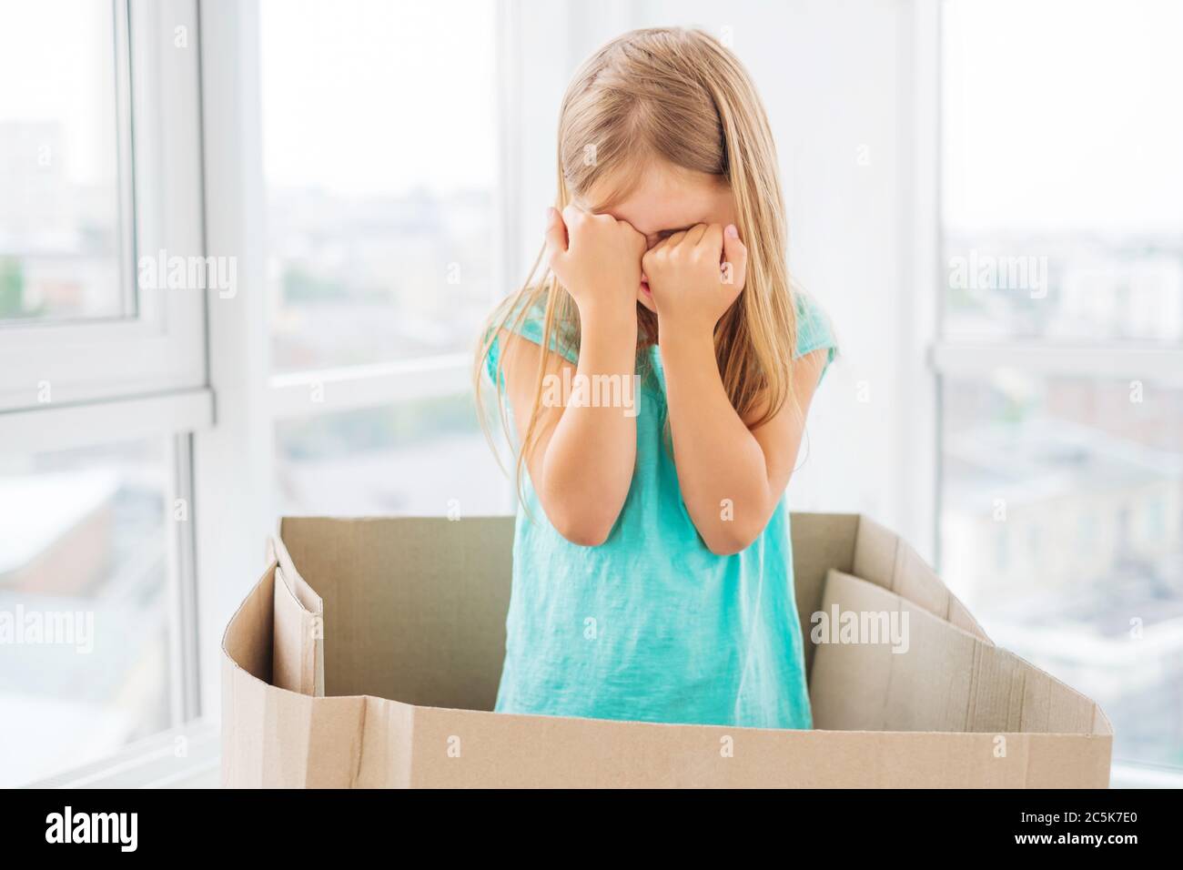 Modellare la bambina mostrando espressioni, coprendo il viso con le mani, in piedi nella scatola Foto Stock