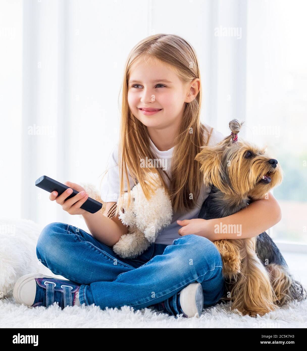 Carina ragazza e il suo cane che cambia canali con il telecomando tv Foto Stock