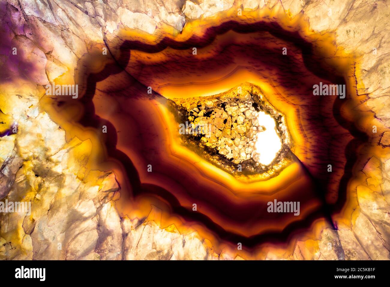 Foto macro di una fetta colorata di agata viola e gialla. L'ho illuminato dal basso per far rischiare le texture minerali e i colori del cristallo. Foto Stock