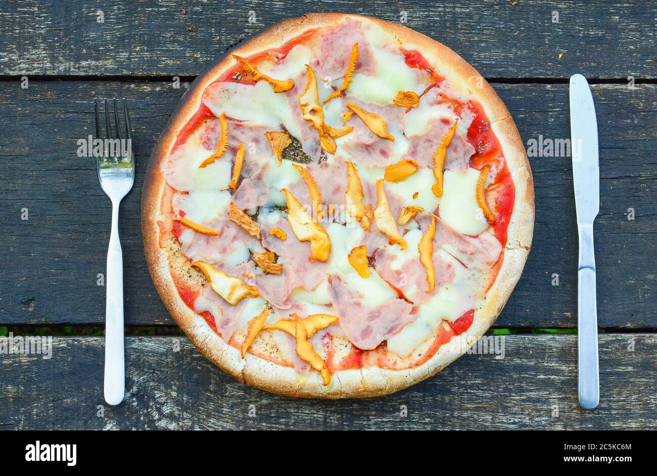 Pizza Chanterelle appena sfornata con forchetta e coltello su vecchio tavolo di quercia grunge Foto Stock