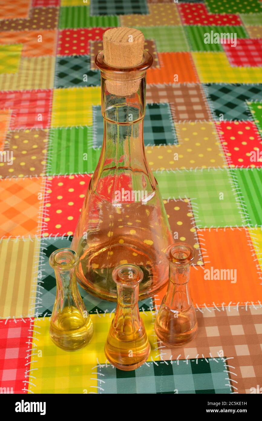 Brandy di prugne vecchio nella bottiglia e tre bicchieri di shot sul tavolo coperto da olio di strofinio macchiato, vista da un lato e dall'altro Foto Stock