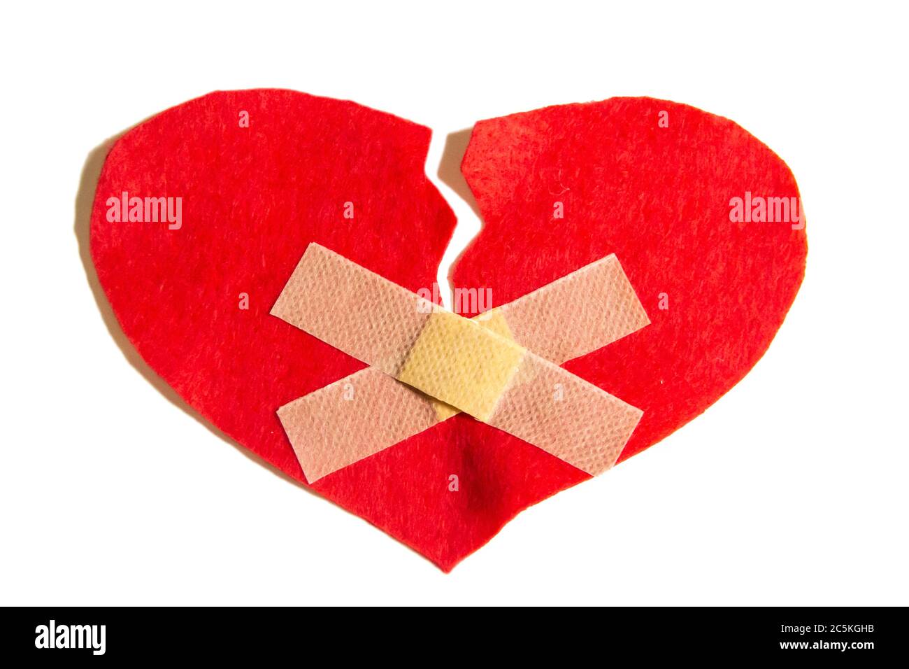 Cuore rotto e incollato insieme con un aiuto-banda. Un cuore dal feltro. Un concetto di amore rotto. Cuore con intonaco isolato su sfondo bianco Foto Stock