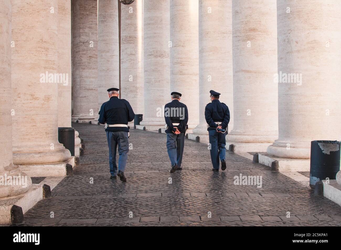 3 poliziotti camminano sul posto di San Pietro a Roma , visto dal retro sotto colonne con le mani sulla schiena Foto Stock