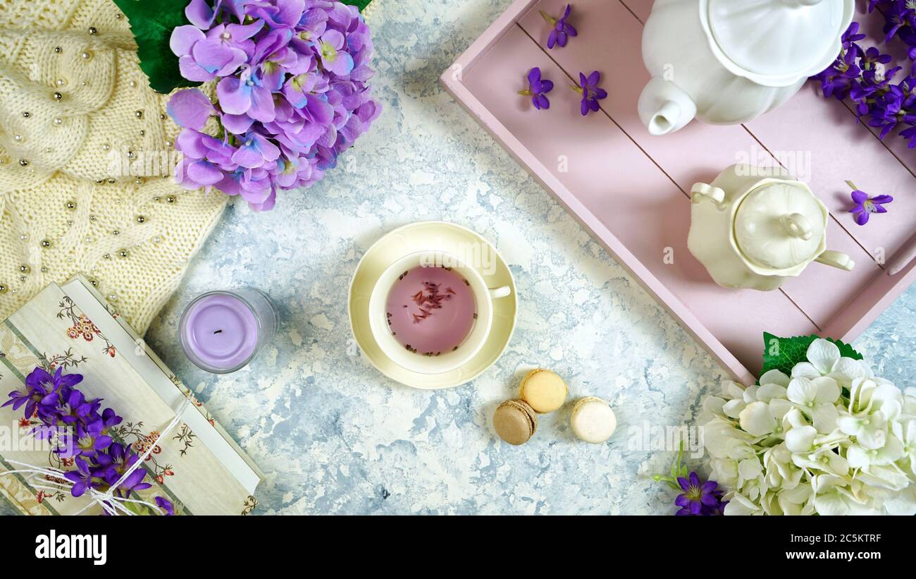Rilassarsi a casa con tè alla lavanda in stile igge e vassoio, libri antichi e un maglione accogliente su sfondo bianco testurizzato. Vista dall'alto della composizione creativa piatta Foto Stock