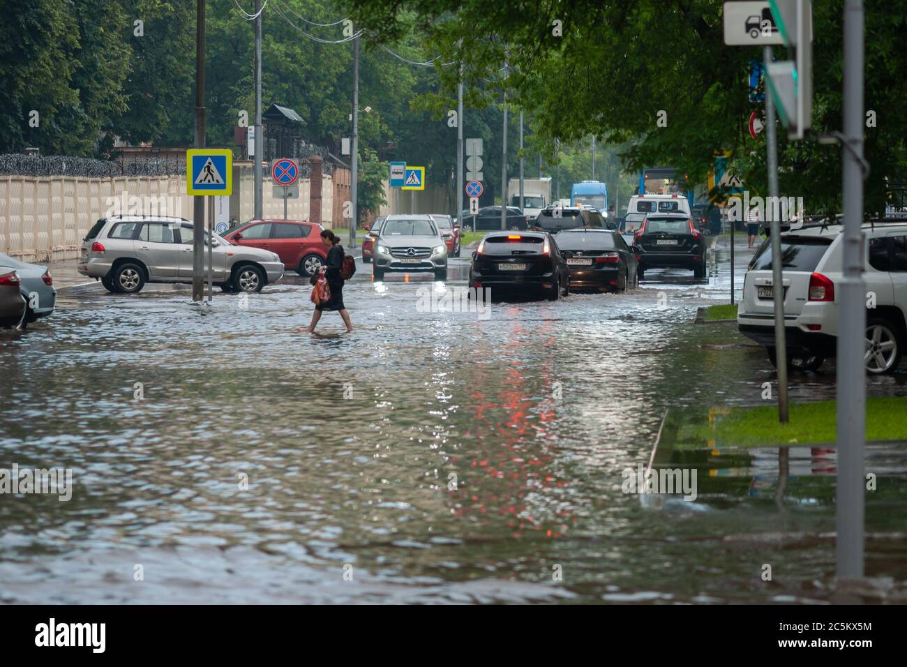 Mosca 18/06/2020 Donna che attraversa la strada allagata di acqua dopo la pioggia pesante, le auto che attraversano l'alluvione Foto Stock