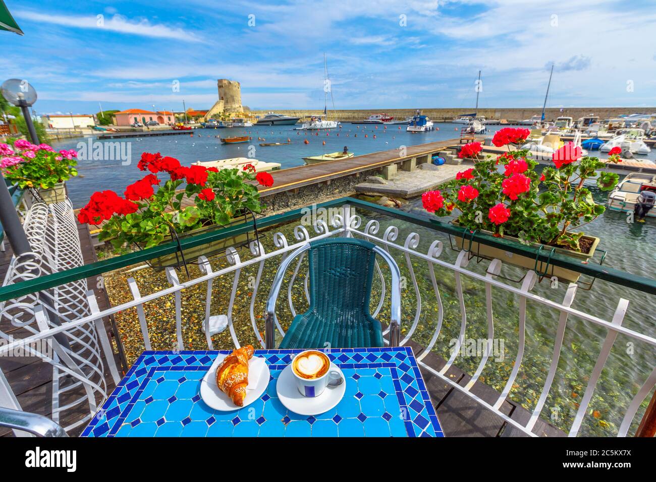 Paesaggio panoramico di gerani rossi fioriti e colazione con croissant e cappuccino in caffetteria italiana. Popolare località balneare Marciana Marina in Foto Stock