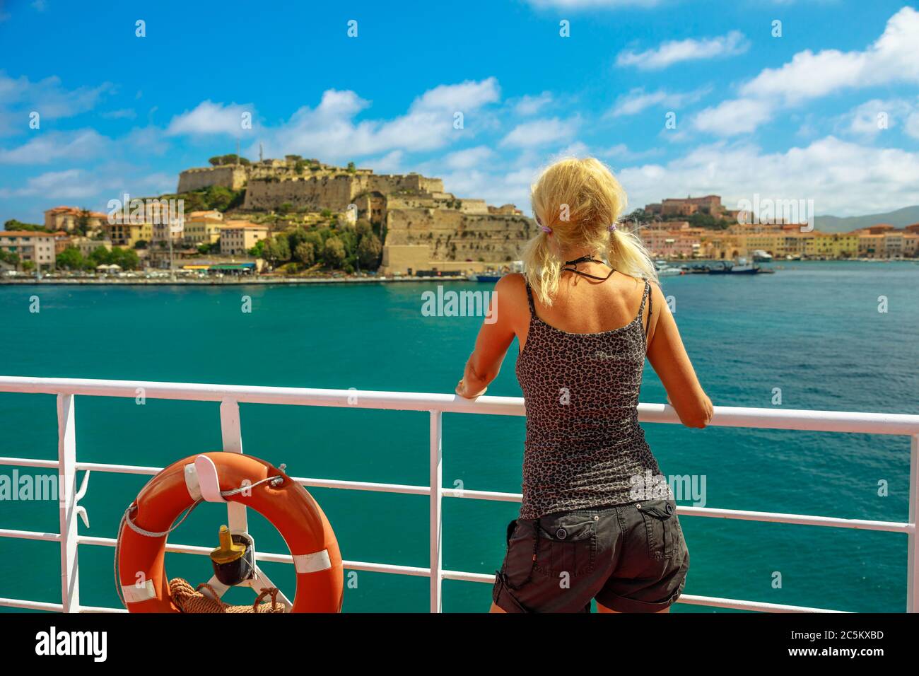 Donna caucasica che guarda Portoferraio porto cittadino su traghetto per l'Isola d'Elba. La donna turistica italiana viaggia all'Elba. Vacanze in Italia, Europa Foto Stock