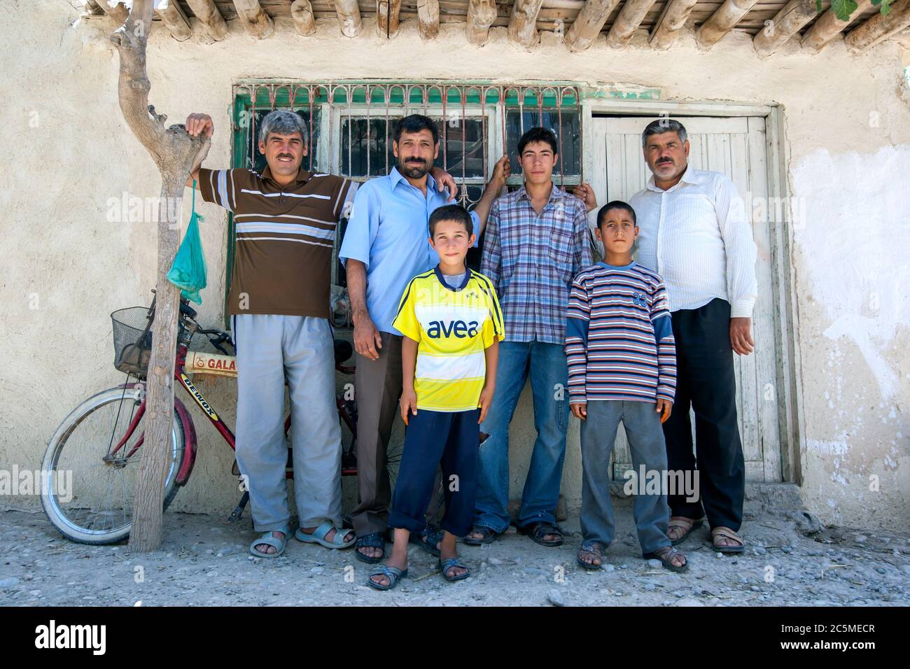 Uomini e ragazzi curdi stare all'ombra in un caldo giorno estati di fronte a una casa nel villaggio di Samsat, nella Turchia orientale. Foto Stock